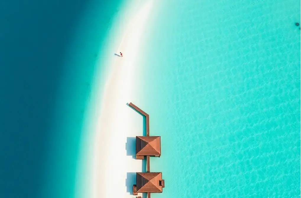 Luftbild einer Sandbank mit Villen über dem Meer in einer türkisfarbenen Lagune der Malediven