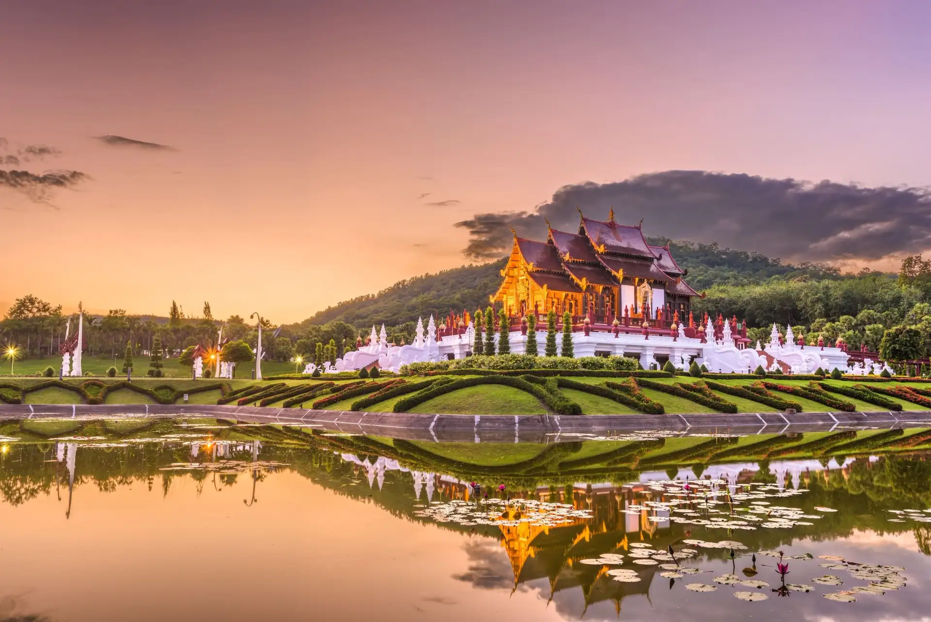 Traditioneller Lanna-Tempel in Chiang Mai bei Sonnenuntergang mit Spiegelung im Wasser und angelegten Gärten.